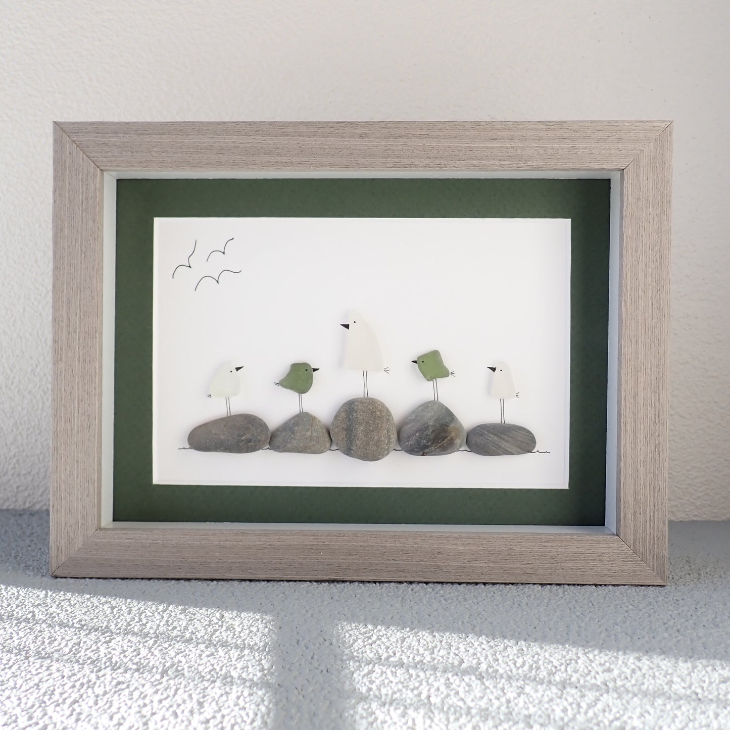 framed picture of six white or green colored sea glass birds sitting on beach rocks