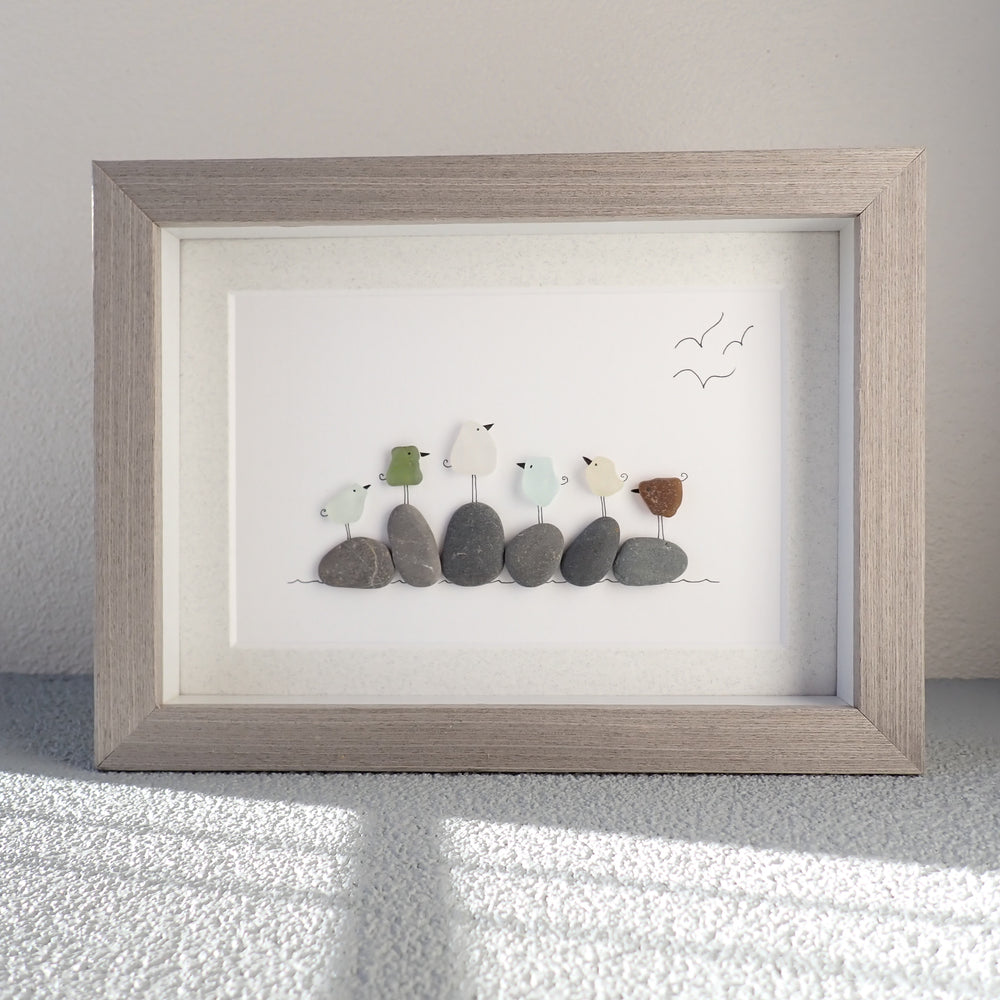 
                  
                    framed picture of six different colored sea glass birds sitting on  beach rocks
                  
                