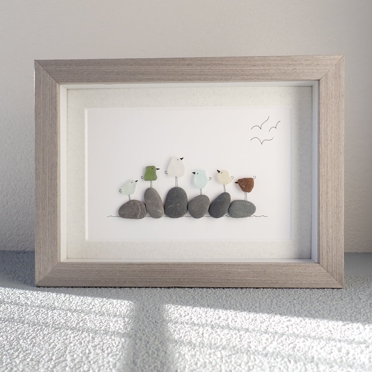 framed picture of six different colored sea glass birds sitting on  beach rocks