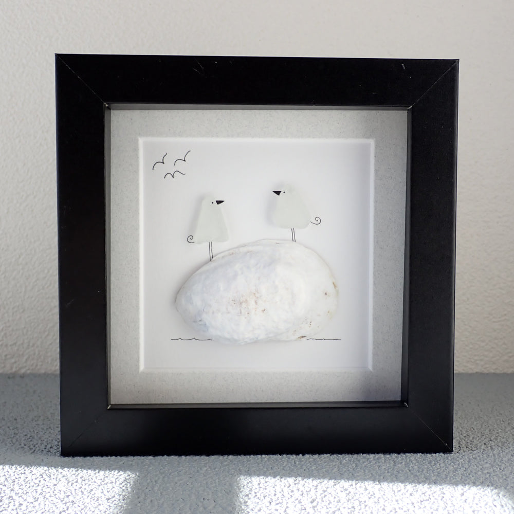 
                  
                    framed picture of two sea glass birds sitting on a white shell
                  
                