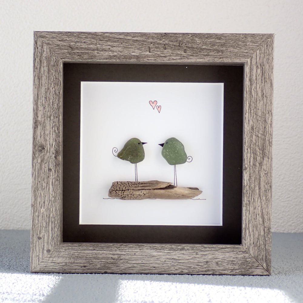 
                  
                    framed picture of two green sea glass birds sitting on a piece of driftwood
                  
                