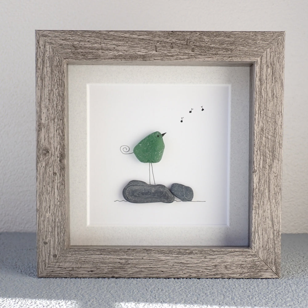 
                  
                    framed picture of green sea glass bird standing on rocks singing
                  
                