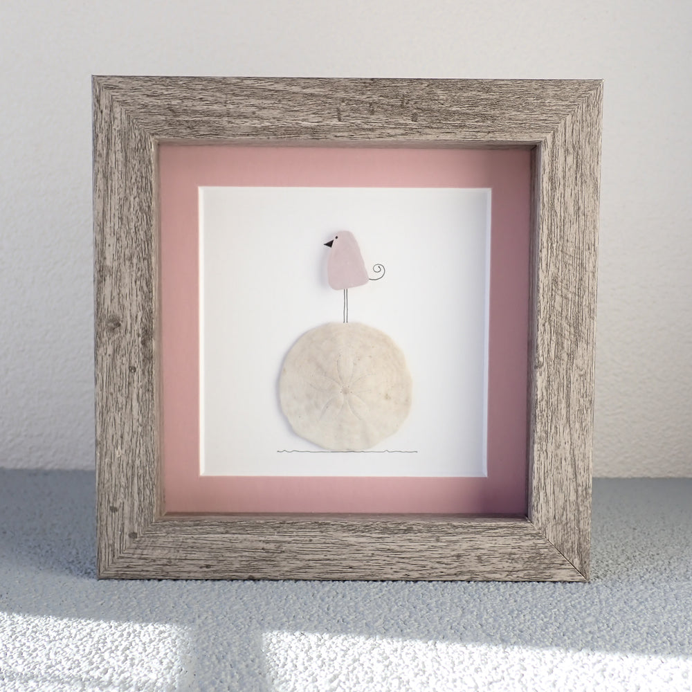 framed picture of a sea glass bird standing on a whole sand dollar