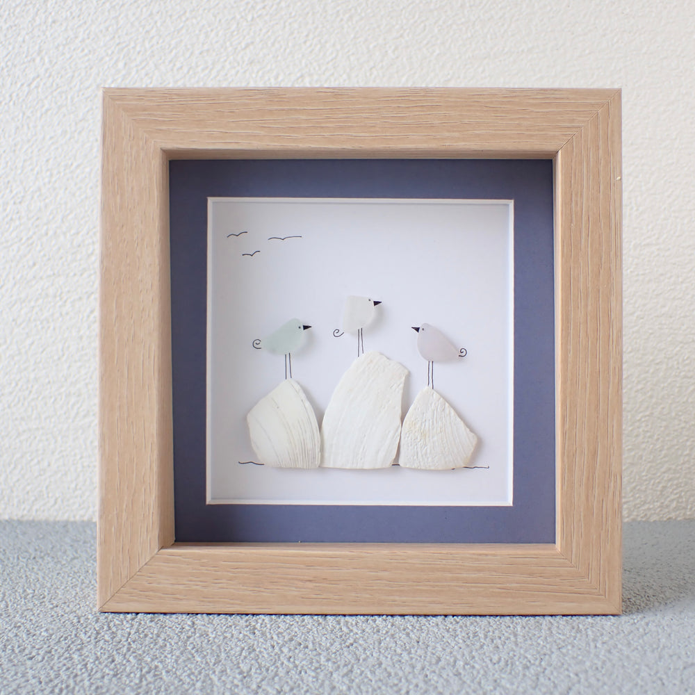 framed picture of Three Colorful Sea Glass Birds on Washed shells and coral