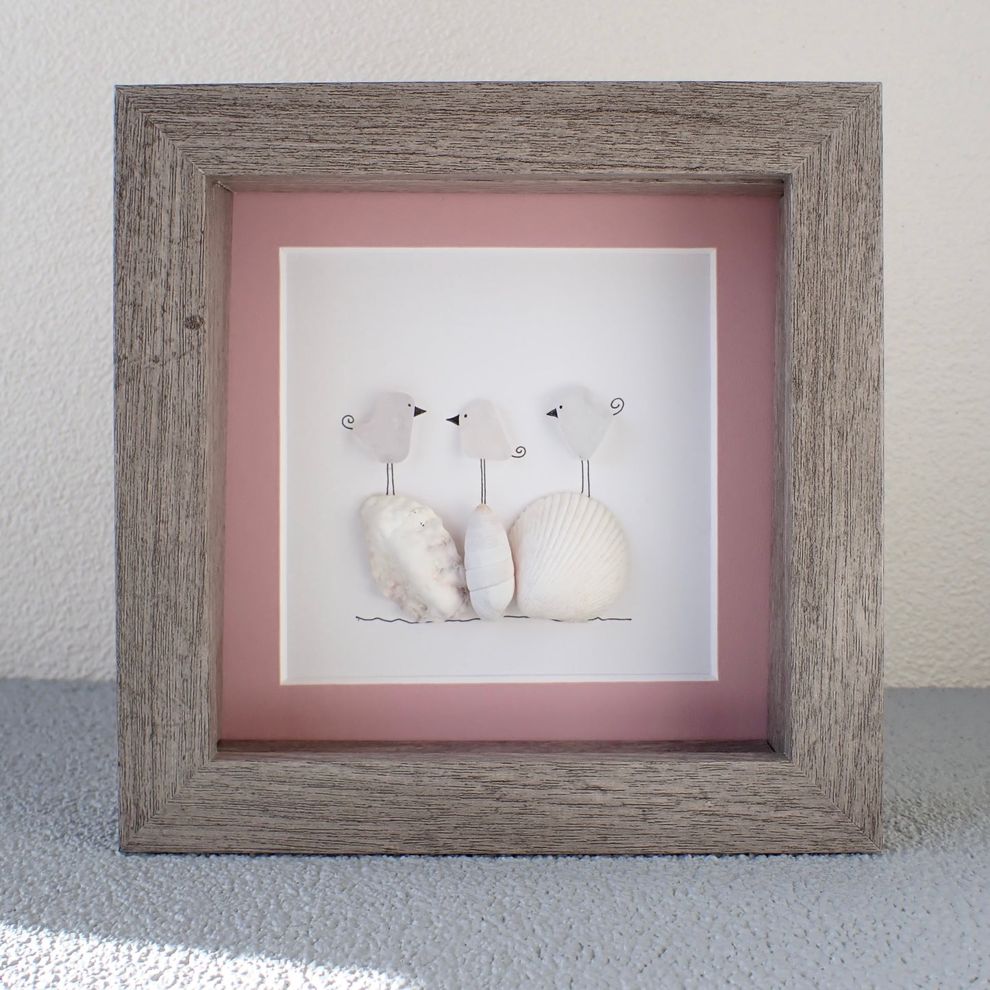 framed picture of three birds standing on washed shells and coral.