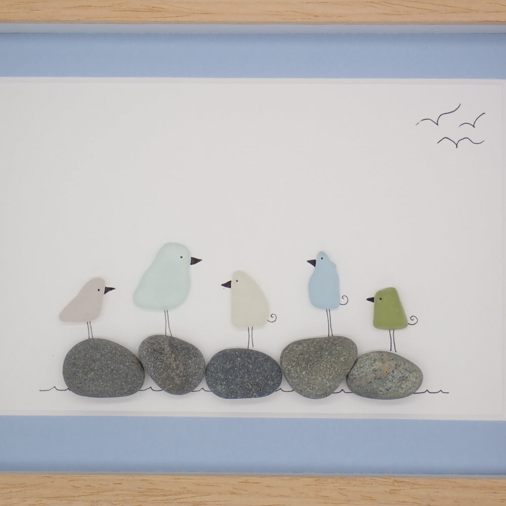 This piece of sea glass art features five colorful glass birds standing on washed pebbles.