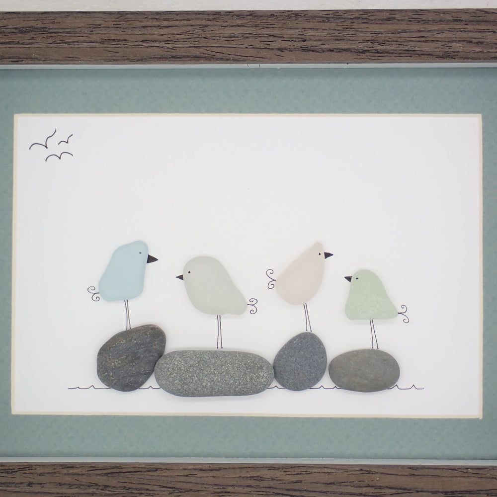 This piece of sea glass art features four different colored glass birds standing on washed pebbles.