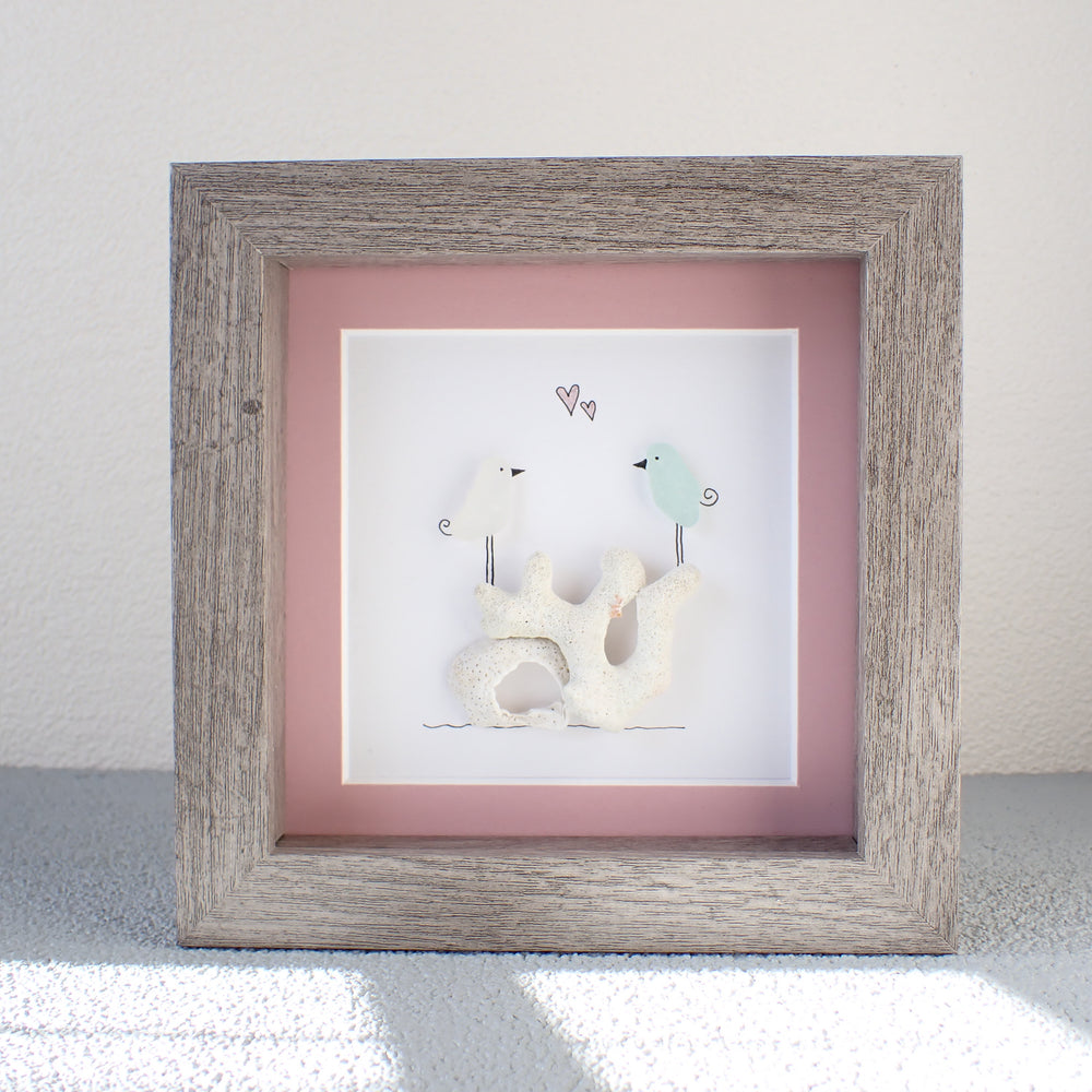 
                  
                    framed picture of two sea glass birds standing on coral
                  
                