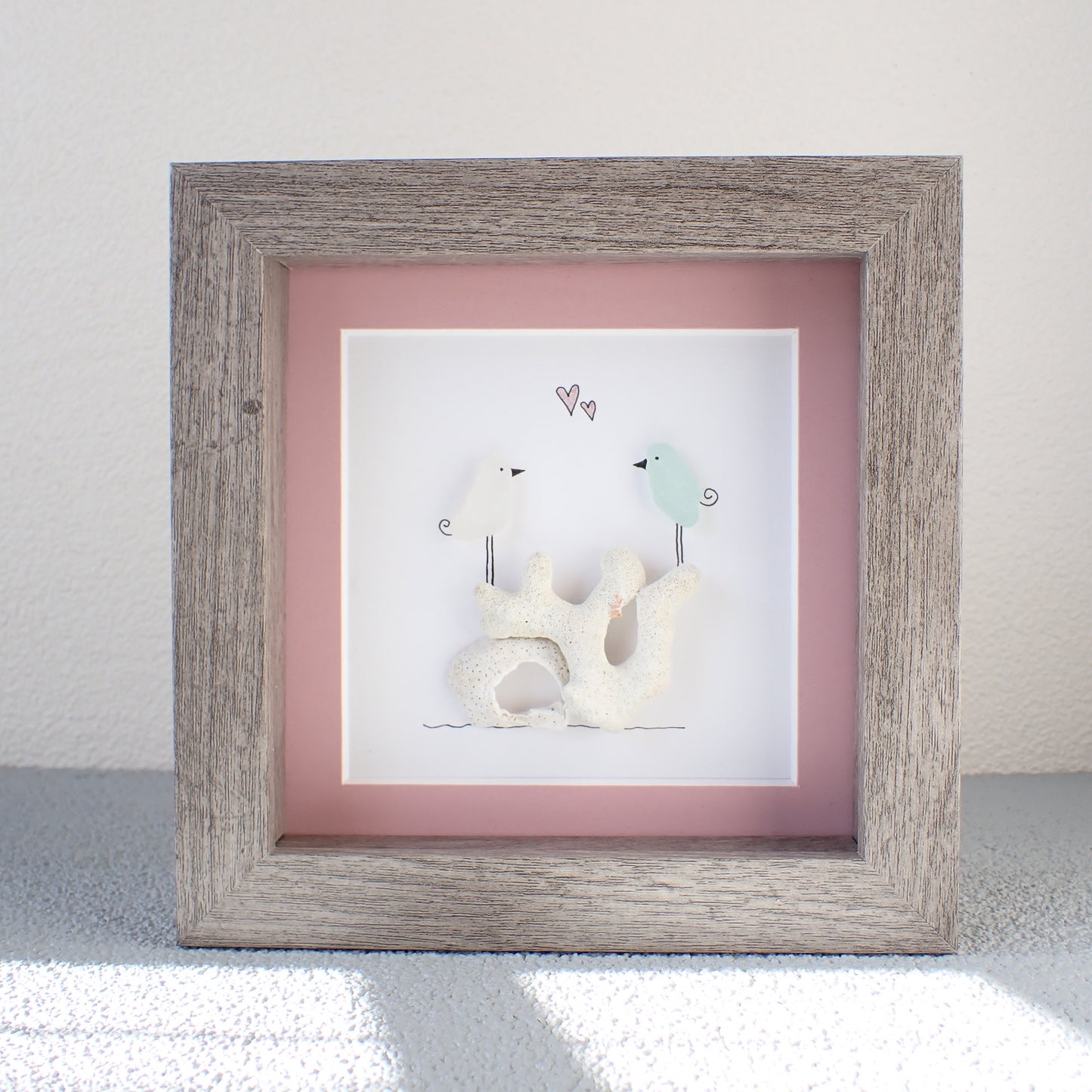 framed picture of two sea glass birds standing on coral