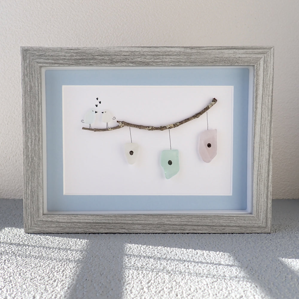 shadowbox frame with a picture of two love birds standing on a branch above three sea glass houses