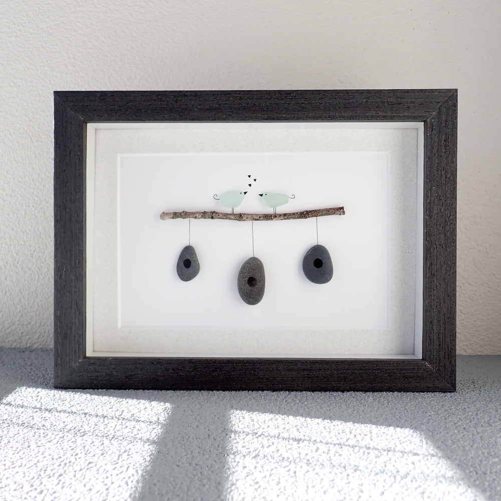 
                  
                    two aqua sea glass birds on a branch with rock bird houses in a black wood shadowbox 
                  
                