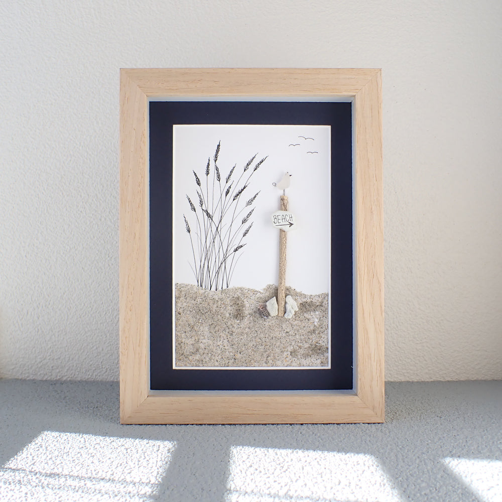 natural shadowbox frame with a hand drawn beach grass, natural sand and a post with a sea glass bird