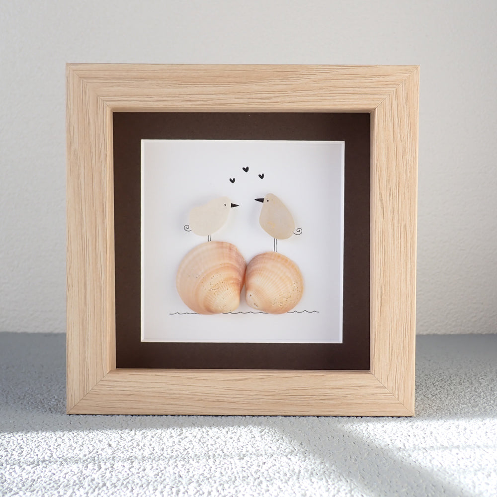 framed picture of two sea glass birds in love standing on orange shells