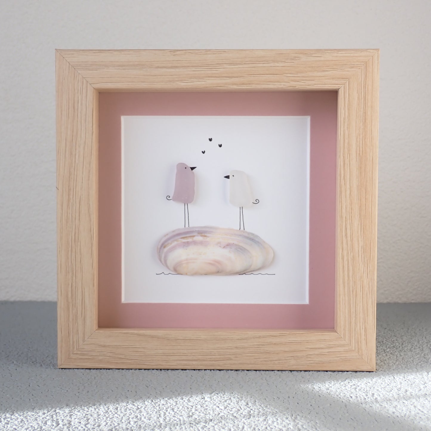 framed picture of sea glass art with love birds standing on a shell.