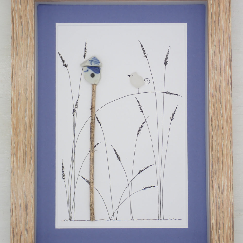 sea glass art features a sea glass bird standing on marsh reeds next to a pottery bird house.