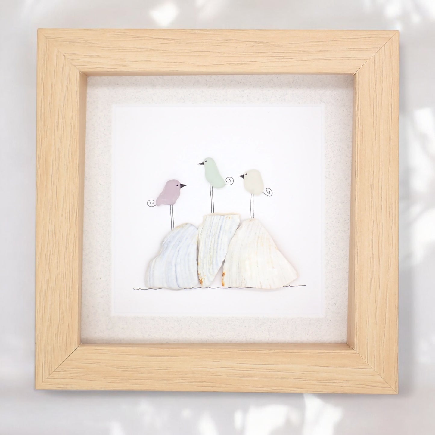 This piece of sea glass art features three colorful birds standing on clam shell pieces.