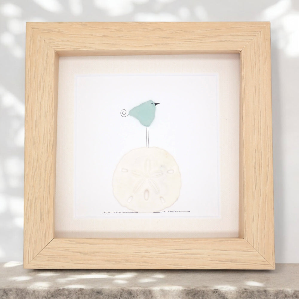 This piece of sea glass art features a bird standing on a sand dollar.