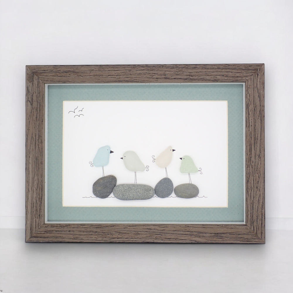 This piece of sea glass art features four different colored glass birds standing on washed pebbles.