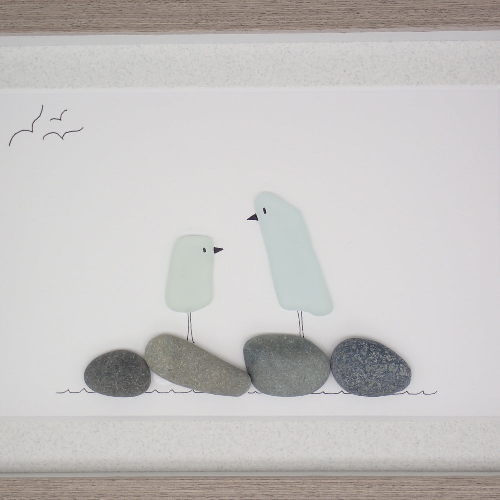 sea glass art features two glass birds standing on beach rocks