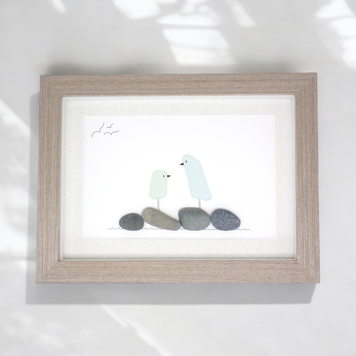 sea glass art features two glass birds standing on beach rocks