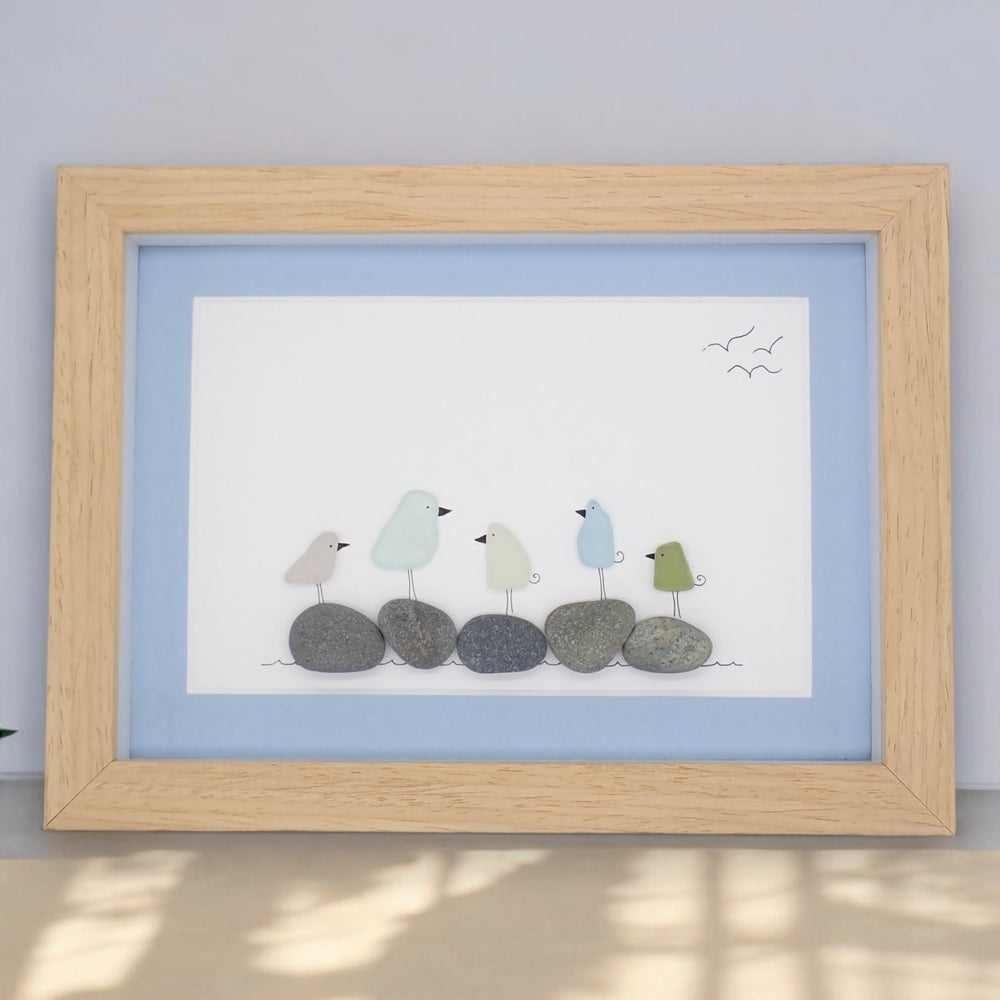 This piece of sea glass art features five colorful glass birds standing on washed pebbles.