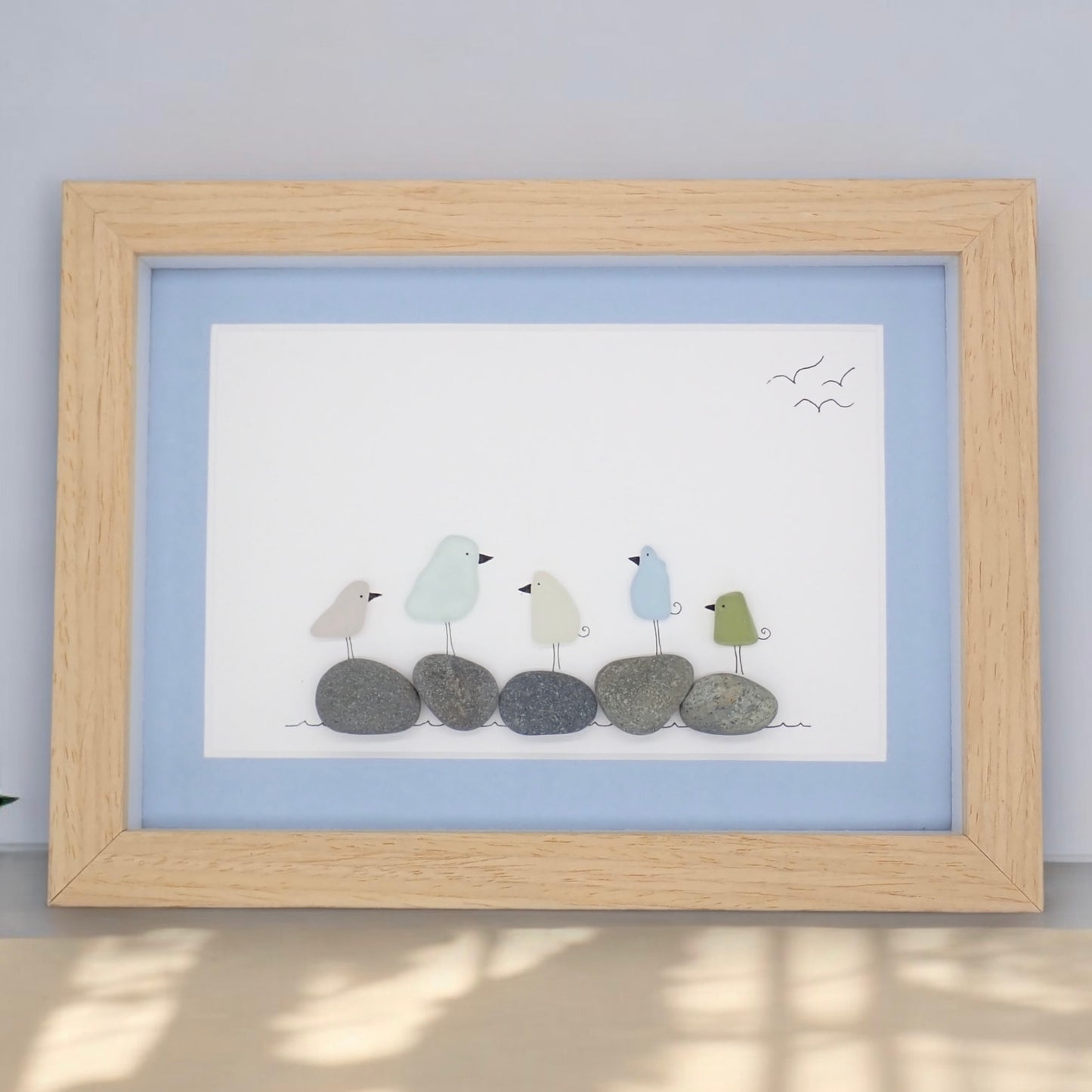 This piece of sea glass art features five colorful glass birds standing on washed pebbles.