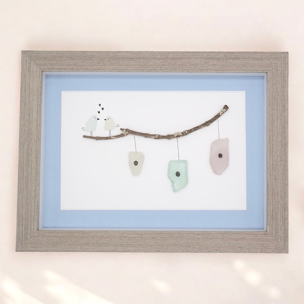 sea glass art features two sea glass birds standing on a branch above bird houses.