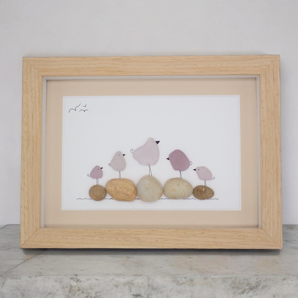 This piece of sea glass art features five purple glass birds standing on washed pebbles.